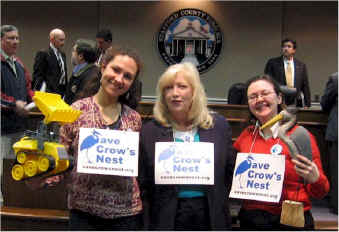 “Save Crow’s Nest” volunteers, Mariel Berrios-Riebe, Helen Stone, and Janette Mason enjoy a lighter moment after the Board of Supervisor meeting where they announced the start of the Crow’s Nest “Report Card,” featuring blue herons (for votes that protect Crow’s Nest) and bulldozers (for votes that facilitate development).